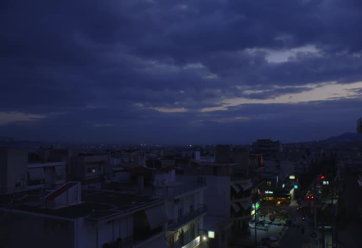 A cityscape with illuminated streets and buildings extends into the distance beneath a dark cloudy sky at dusk or dawn