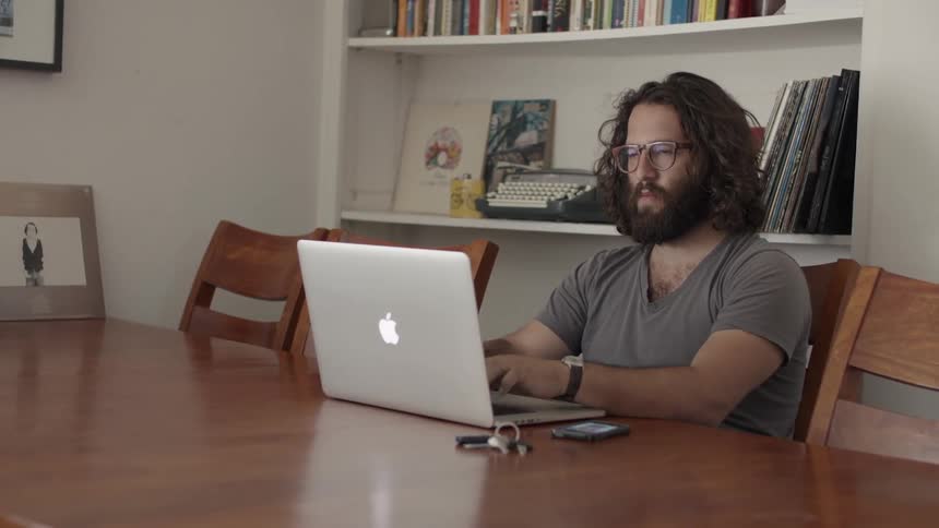 A man sits at a table and works on a laptop