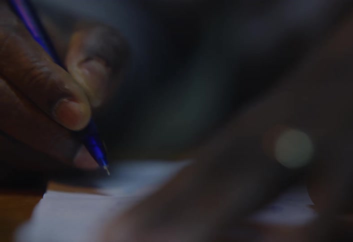 Hands writing on paper with a blue pen in dim lighting