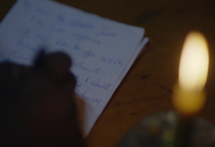 Person writing a note by candlelight in a dark room