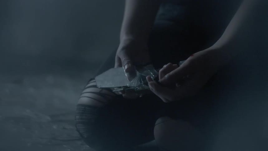 Long-haired woman looking sadly down at reflective pieces of rocks as she slowly drops them