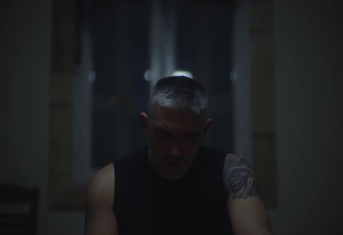 Older man sits indoors at night and thinks while smoking a cigarette