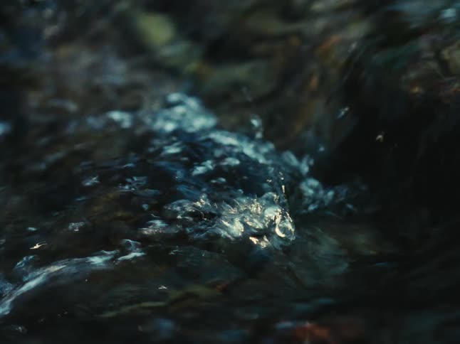 Clear stream water flows over large rocks while moving down a slope