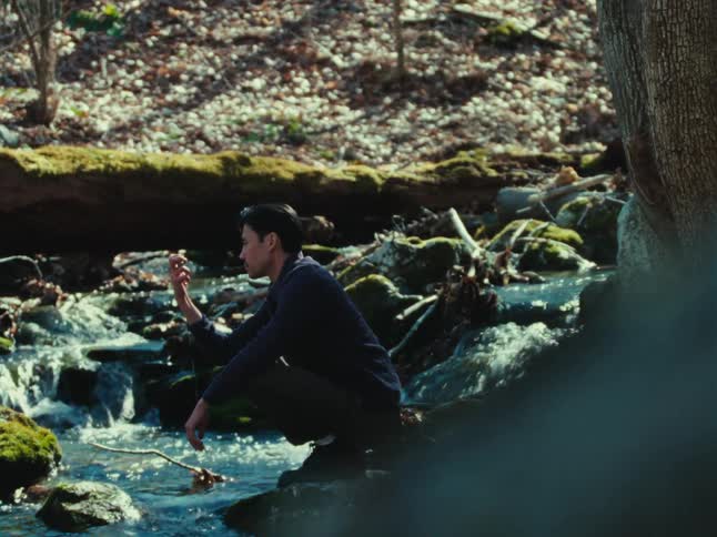 A footage of a man squatting beside the stream