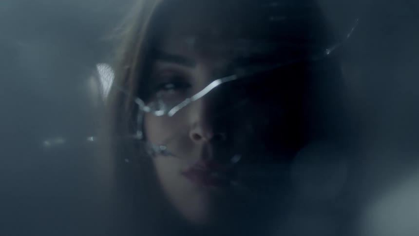 A woman slowly opens her eyes in front of a piece of broken glass