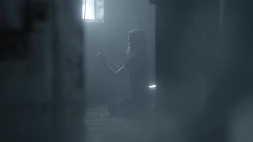 A woman is kneeling in a room looking at something in front of a window