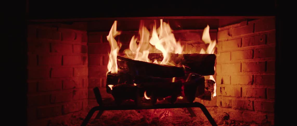 A fire burning brightly in a brick fireplace with flames licking around stacked logs and casting a soft glow on the surrounding hearth