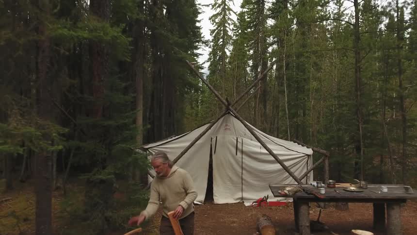 Man walking out of tent and spliting wood with an ax while camping