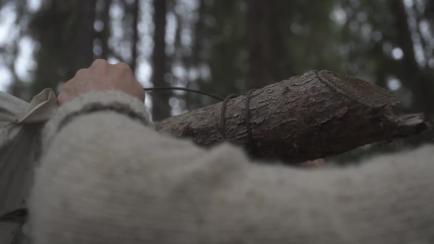 A man unties twine while dismantling a tarp placed over a log disassembling a tent in a forest