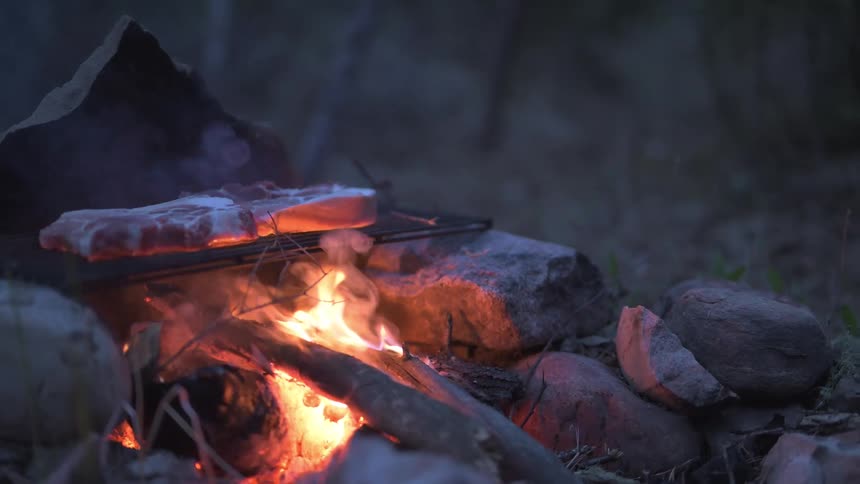The steak cooks on the campfire
