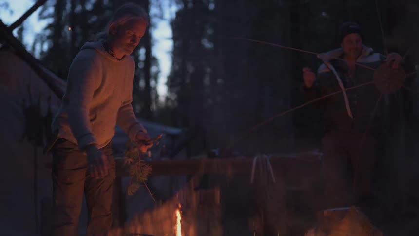 A man tosses branches on the campfire
