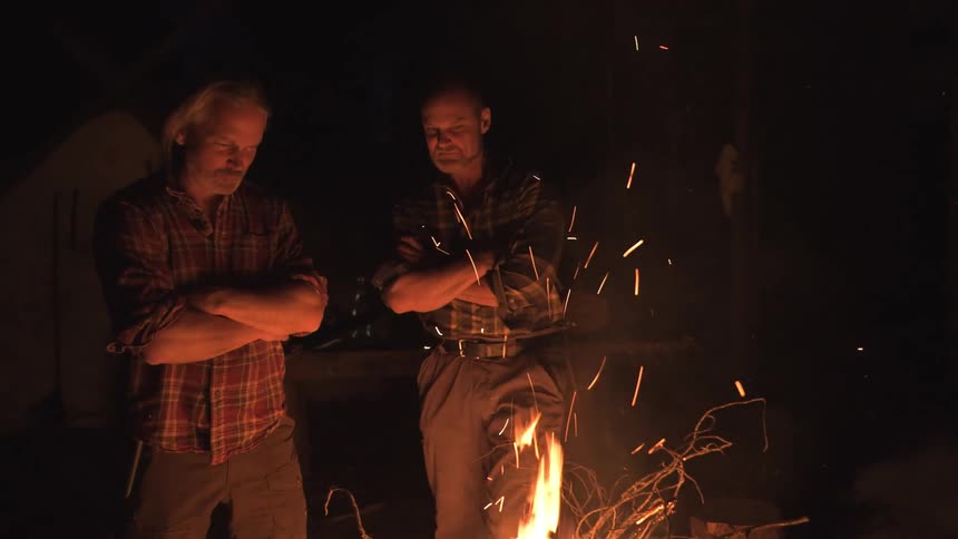 Two men are talking next to a bonfire at night