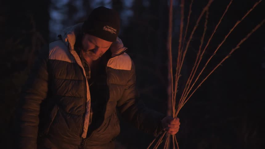 A man is tying a bunch of sticks together to make a trap