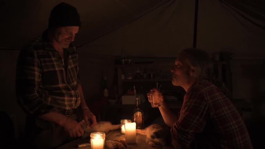 Two men camping talk while they cook and drink