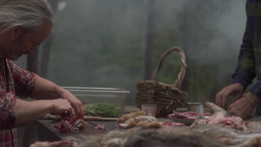Two men are butchering meat on a table