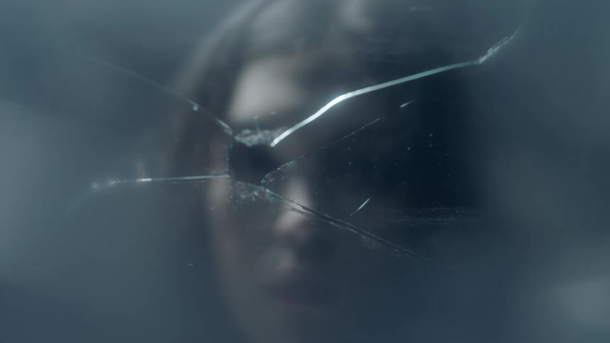 A woman looks through the hole in a broken glass window