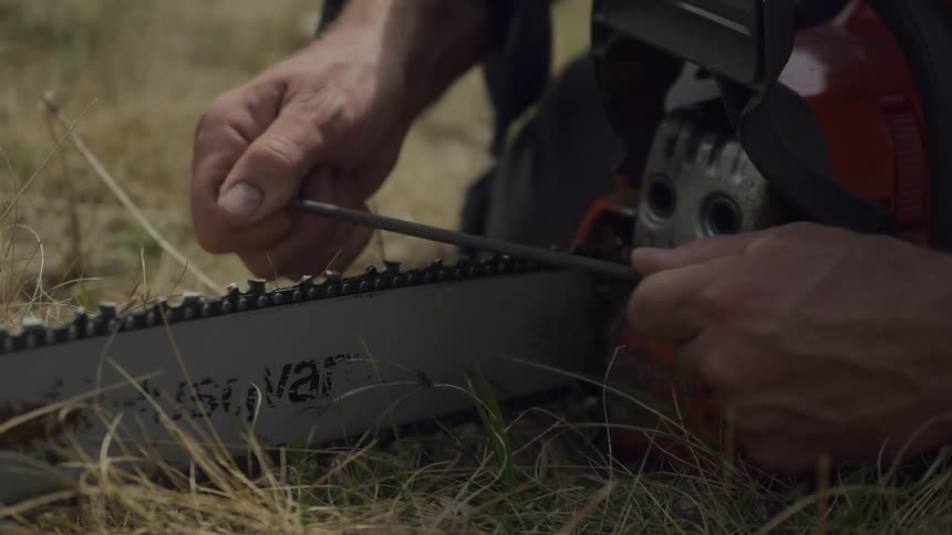 A mans hands are adjusting a chainsaw with the focus on the tool and the act of maintenance