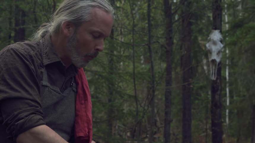 Older man tastes a meal while standing in his campsite in the woods