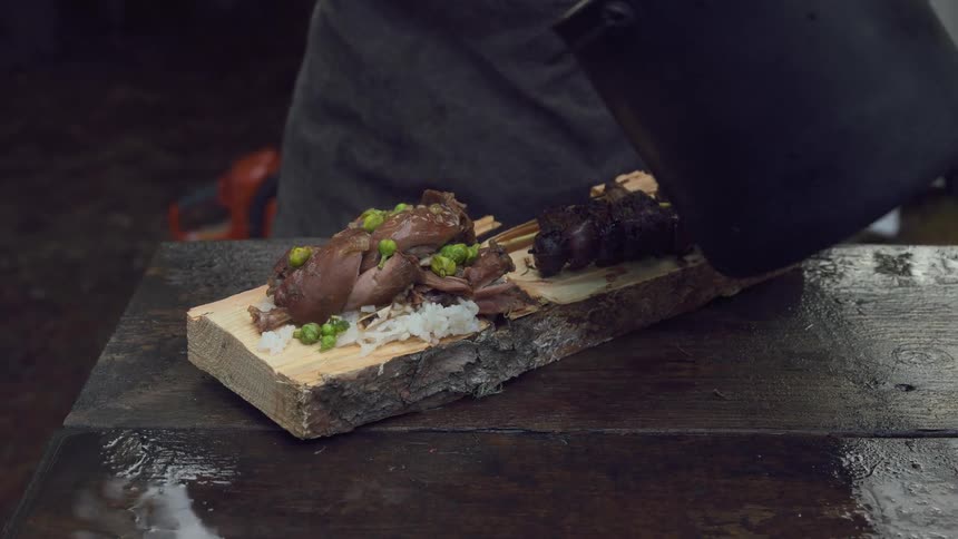 A man is serving food on a piece of wood