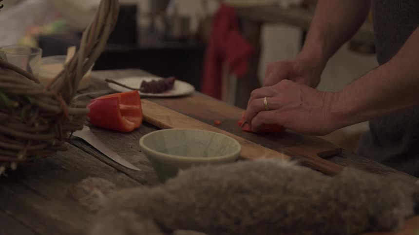 A closeup of a mans hand slicing peppers on a cutting board in a rustic kitchen