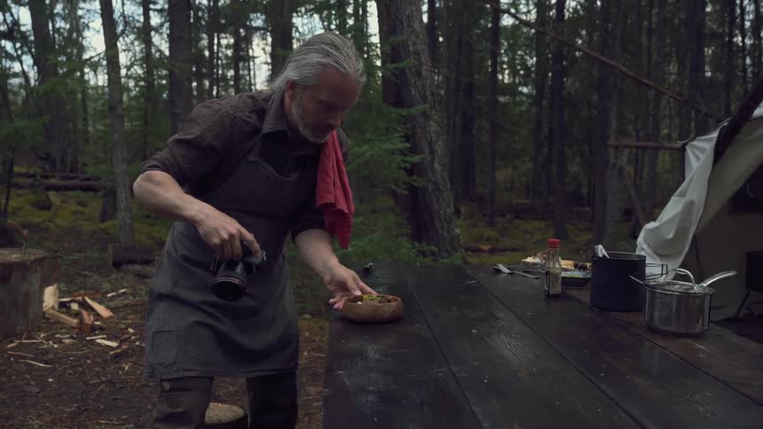 Man takes a picture of a meal while at a camp in the woods