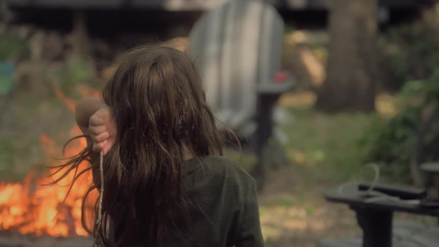 Child walking towards a campfire and throwing a twig in to it