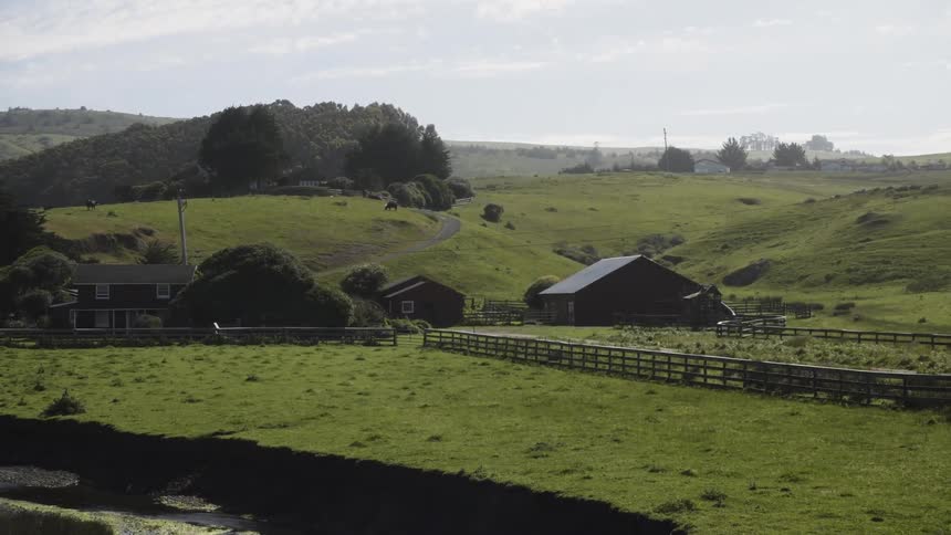 A farm sits near a hilly area on this cloudy day