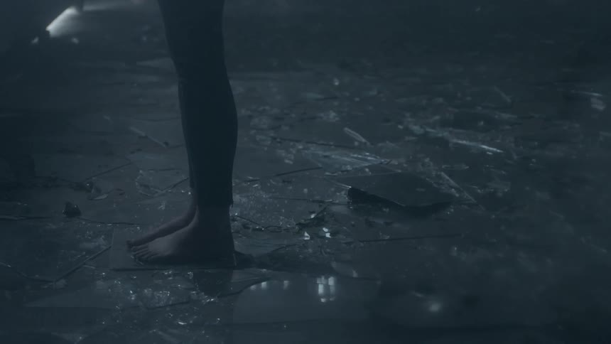 A woman's bare feet are surrounded by shards of glass