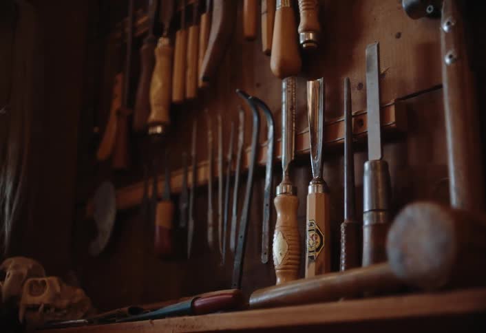 A collection of various woodworking chisels and other hand tools hangs neatly organized on racks and rests on a shelf within a workshop