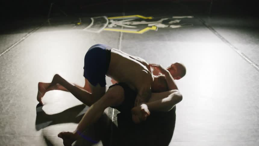 Two men are wrestling each other in an empty gym