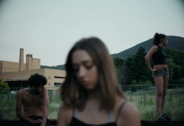 Three teenagers stand casually outdoors near an industrial building standing around in a relaxed manner