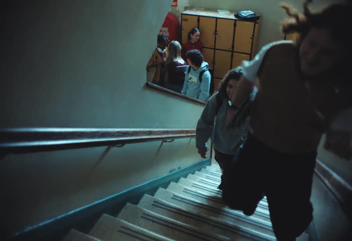 Students are ascending a stairwell in a high school with yellow lockers lining the wall behind them