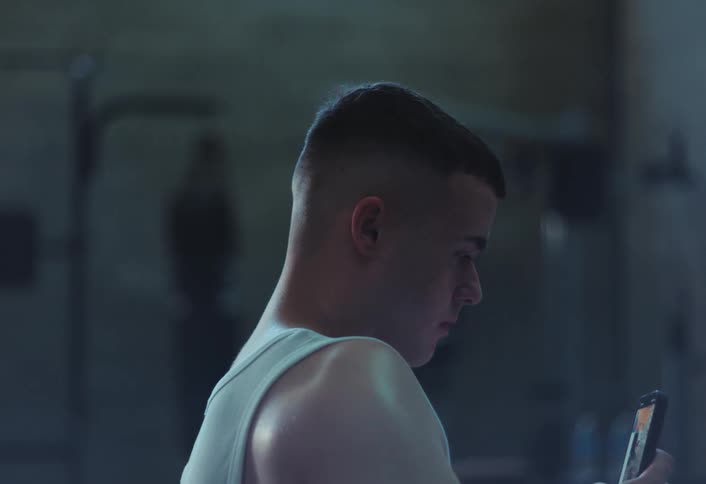 A male is standing in a gym and looking at his cellphone