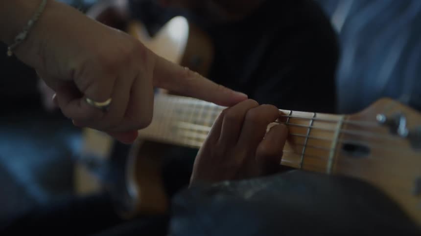 A man teaches a boy to play an acoustic guitar while sitting on a couch at home