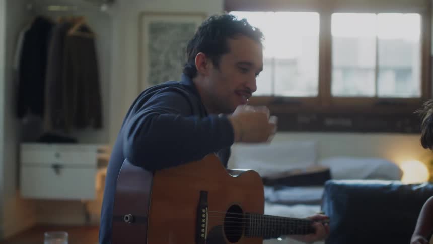 Adult guitarist instructs a child in playing a guitar while they sit in the living room
