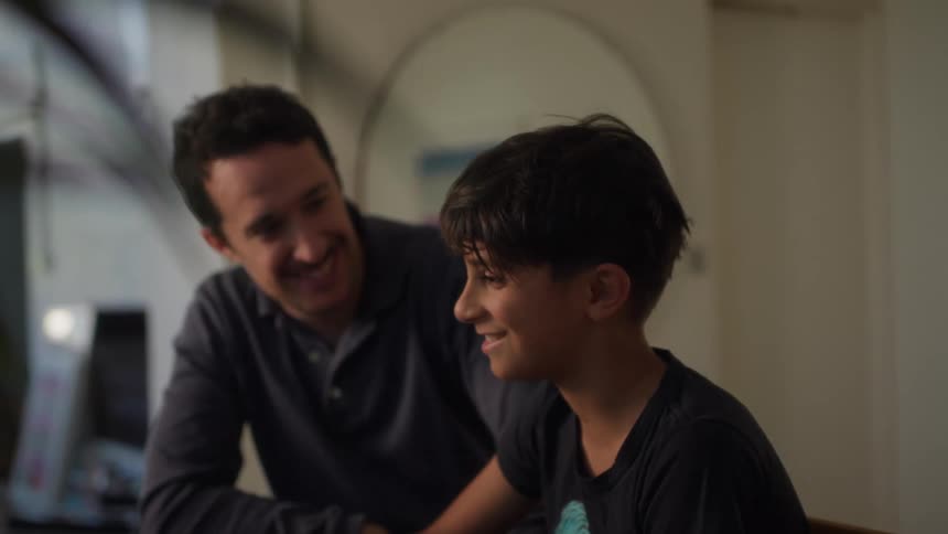 A father and son smile and talk while looking at a laptop