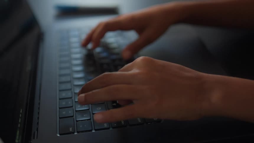 A closeup of a childs hands typing on a laptop at a table in their home