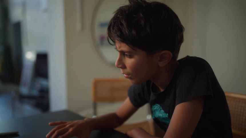 A young boy with dark hair and a black t shirt is focused on a laptop screen