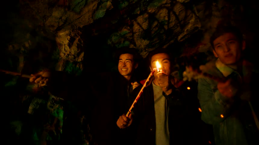 A group of friends ignite fireworks inside a cave creating vivid bursts of colorful light against the surrounding darkness