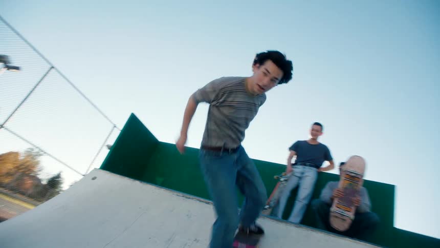A young man skateboards on a u ramp while friends watch from above at a skatepark on a sunny morning