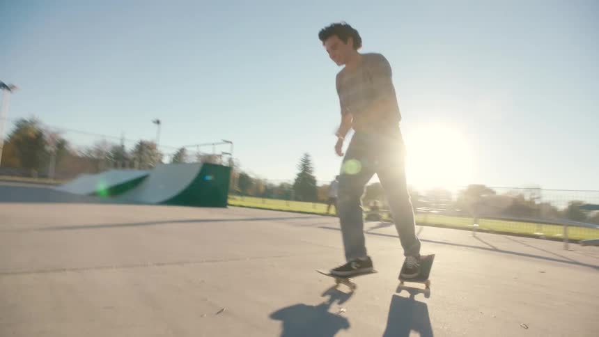 A teenager precariously balances on a skateboard split in half at a skate park under the morning sun