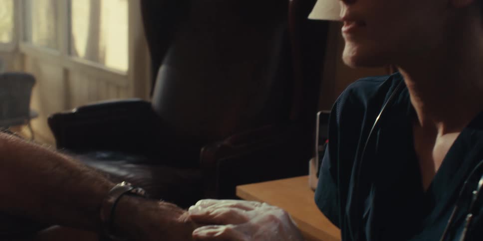 A nurse is holding a mans hand while she talks to him