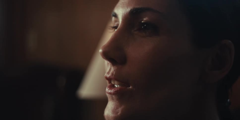A closeup shows a woman speaking in a room at home