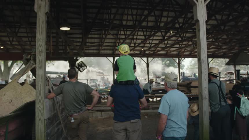 People stand watching craftmen in an open air structure while smoke fills the air