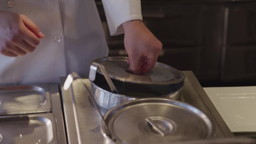 Chef lifting lid and stirring sauce cooking in the pot