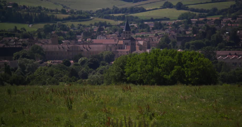 A panoramic view of cluny burgundy france featuring the historic town with its prominent abbey ruins and surrounding buildings nestled in a green rolling landscape under a bright sky