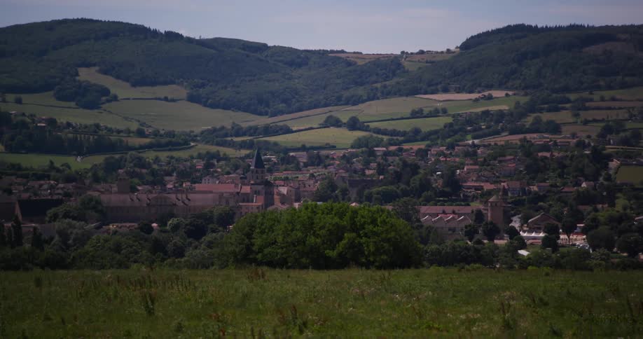 A small village is nestled among trees in a picturesque rural landscape with rolling hills and fields stretching into the distance under a serene sky