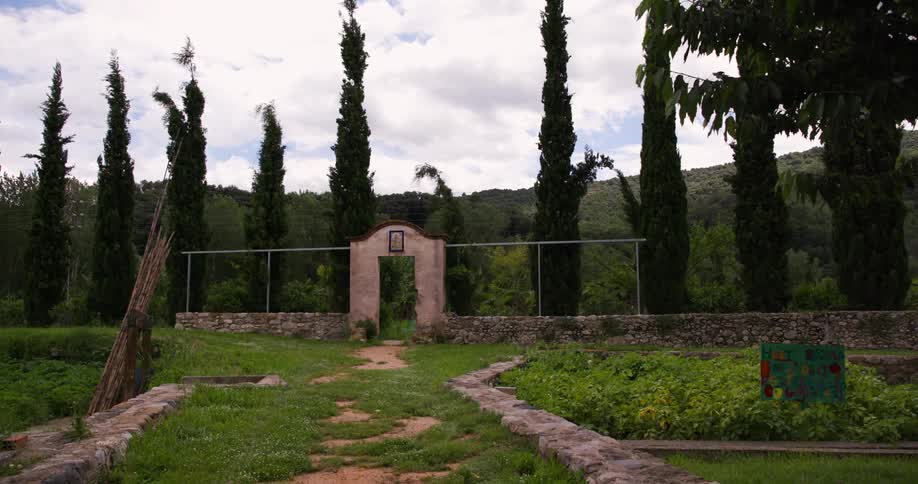 Gateway in a low outdoor wall separates a landscaped yard from a hill on a cloudy day