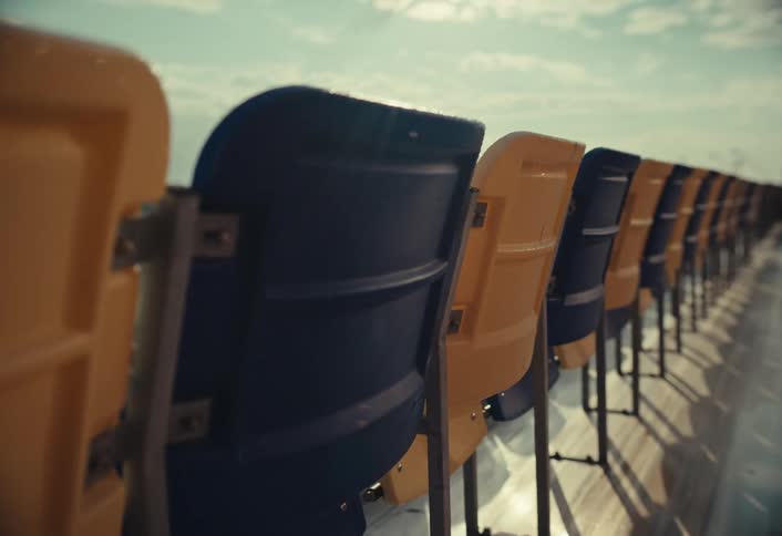 Empty yellow and blue stadium seats overlook a deserted racetrack under a bright sky