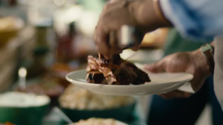 People enjoy an outdoor barbecue on a sunny day serving themselves ribs and salad onto plates